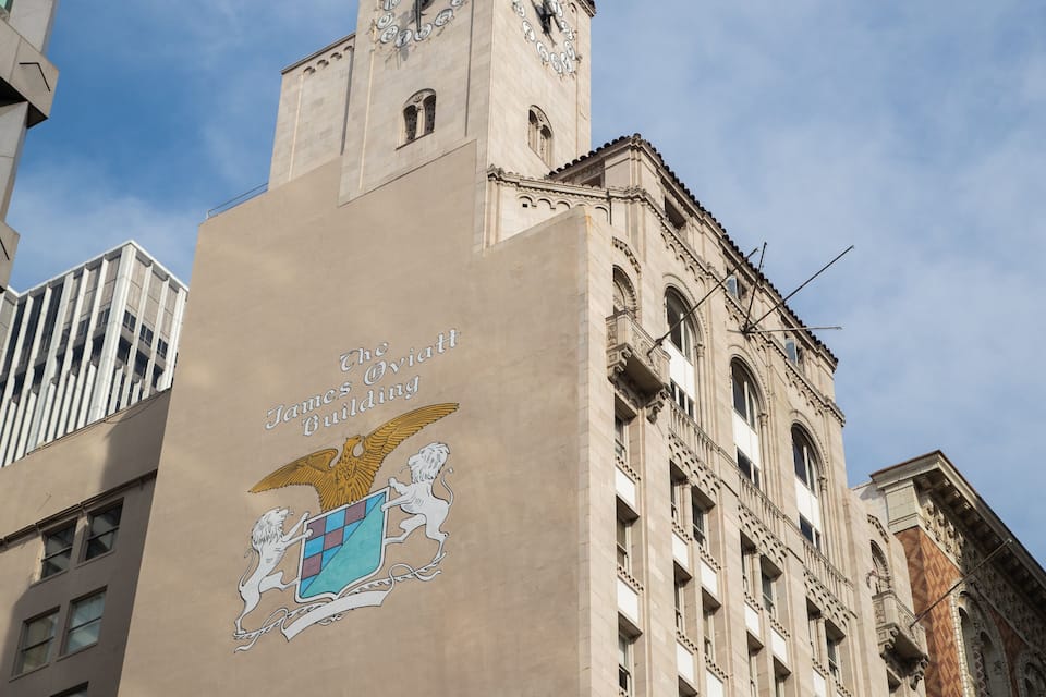 Um edifício com um grande emblema de águia e leão, o Edifício James Webb, com uma torre do relógio e arquitetura clássica.