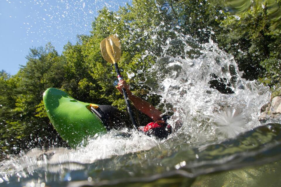A kayaker navigating through a turbulent river surrounded by lush greenery.