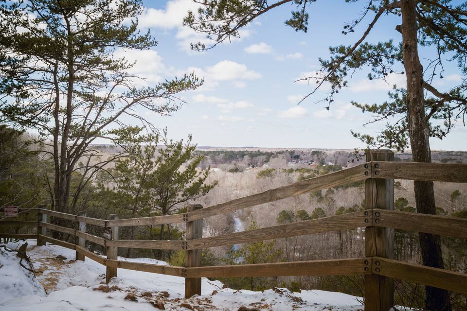 A wooden observation deck overlooking a snowy landscape with trees and a distant view of a canyon.