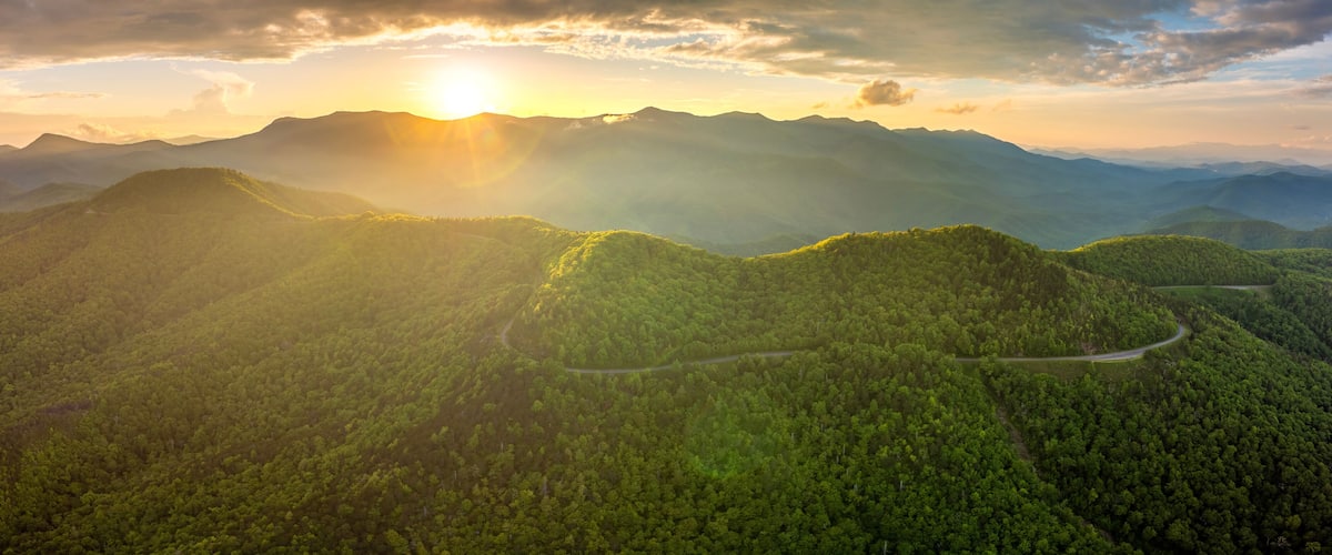 A mountainous landscape with a winding road and dense forest.