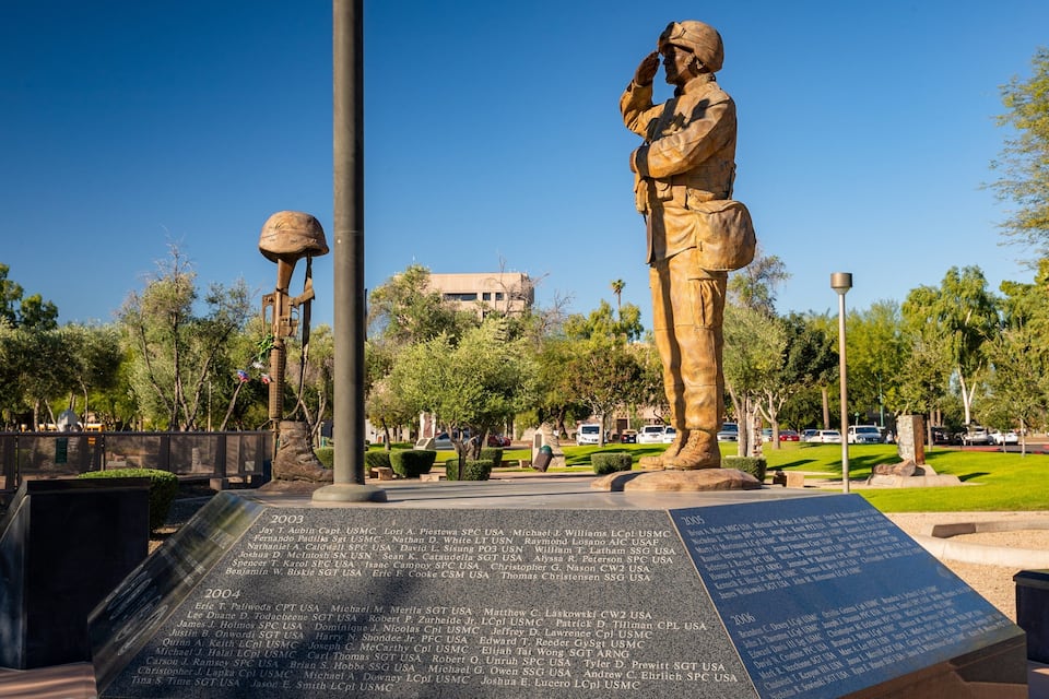 A memorial with a statue of a soldier, a plaque with names, and a lamppost.