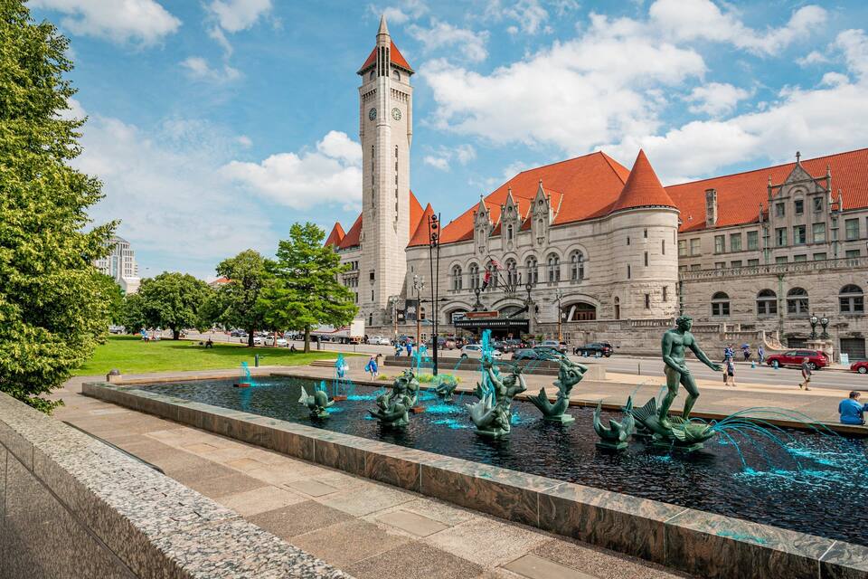 A historic building with a clock tower and a fountain with statues.