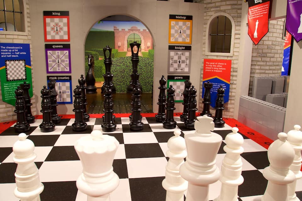 Um tabuleiro de xadrez com peças pretas e brancas em um cenário com tema de castelo.