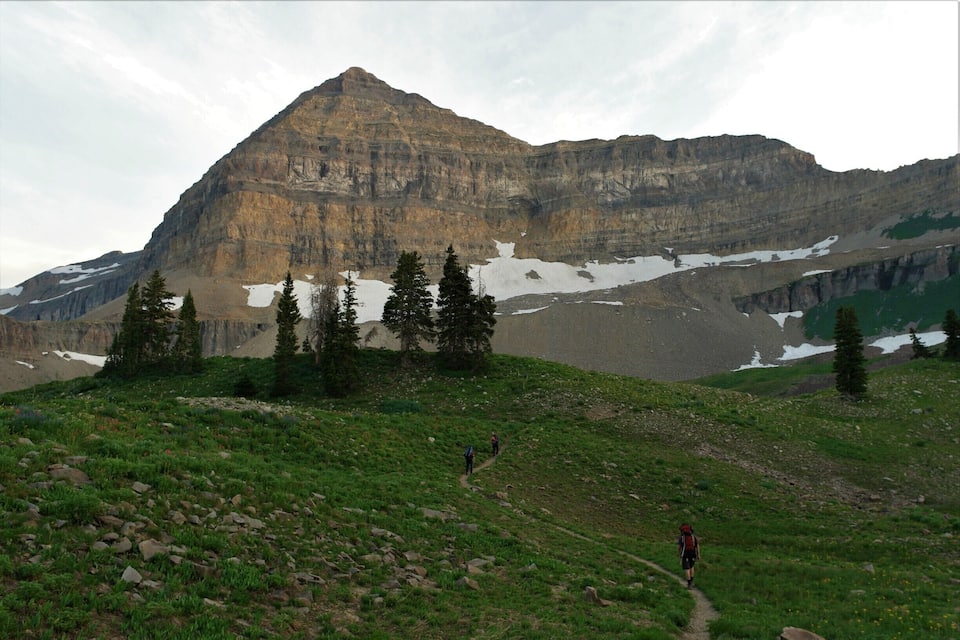 A mountain landscape with a prominent peak, a snow-covered valley, and a trail with hikers.