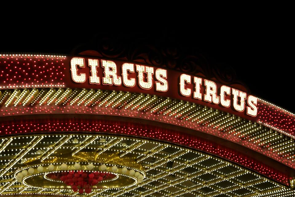 A brightly lit circus sign with red and white lights.