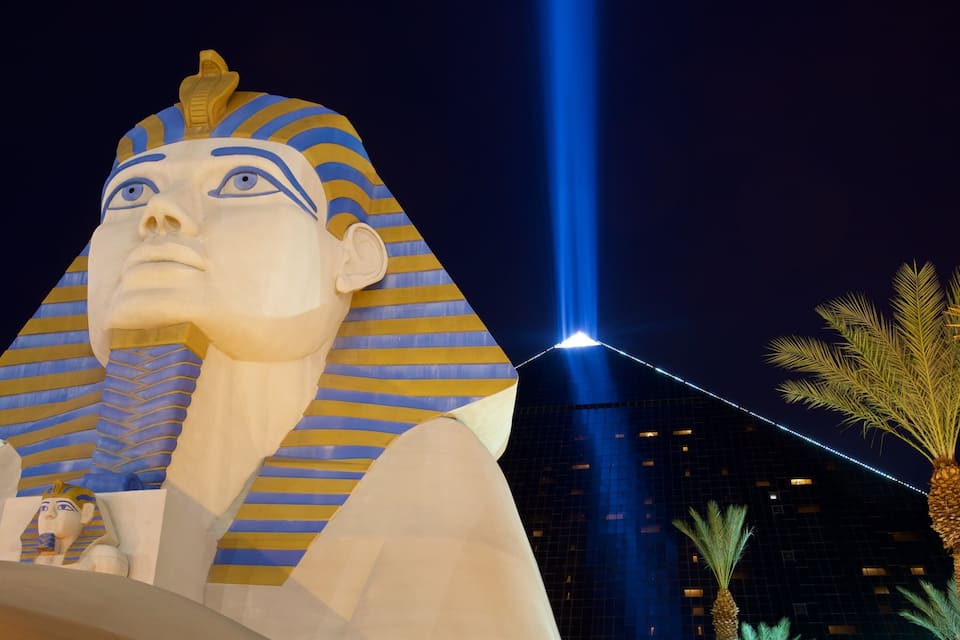 A large, illuminated sphinx statue at night with a blue light beam in the background.