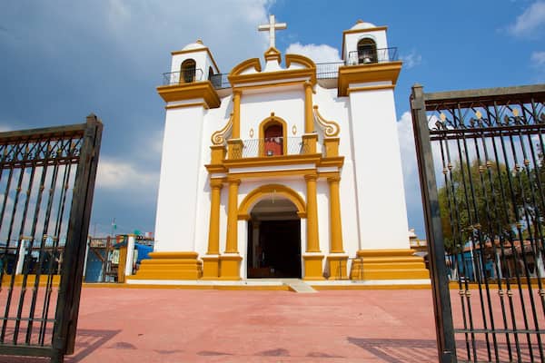 A white and yellow church with a bell tower and a cross on top.
