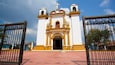 A white and yellow church with a bell tower and a cross on top.
