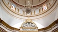 An ornate interior with a large chandelier, golden decorations, and a central statue of an angel holding a child.