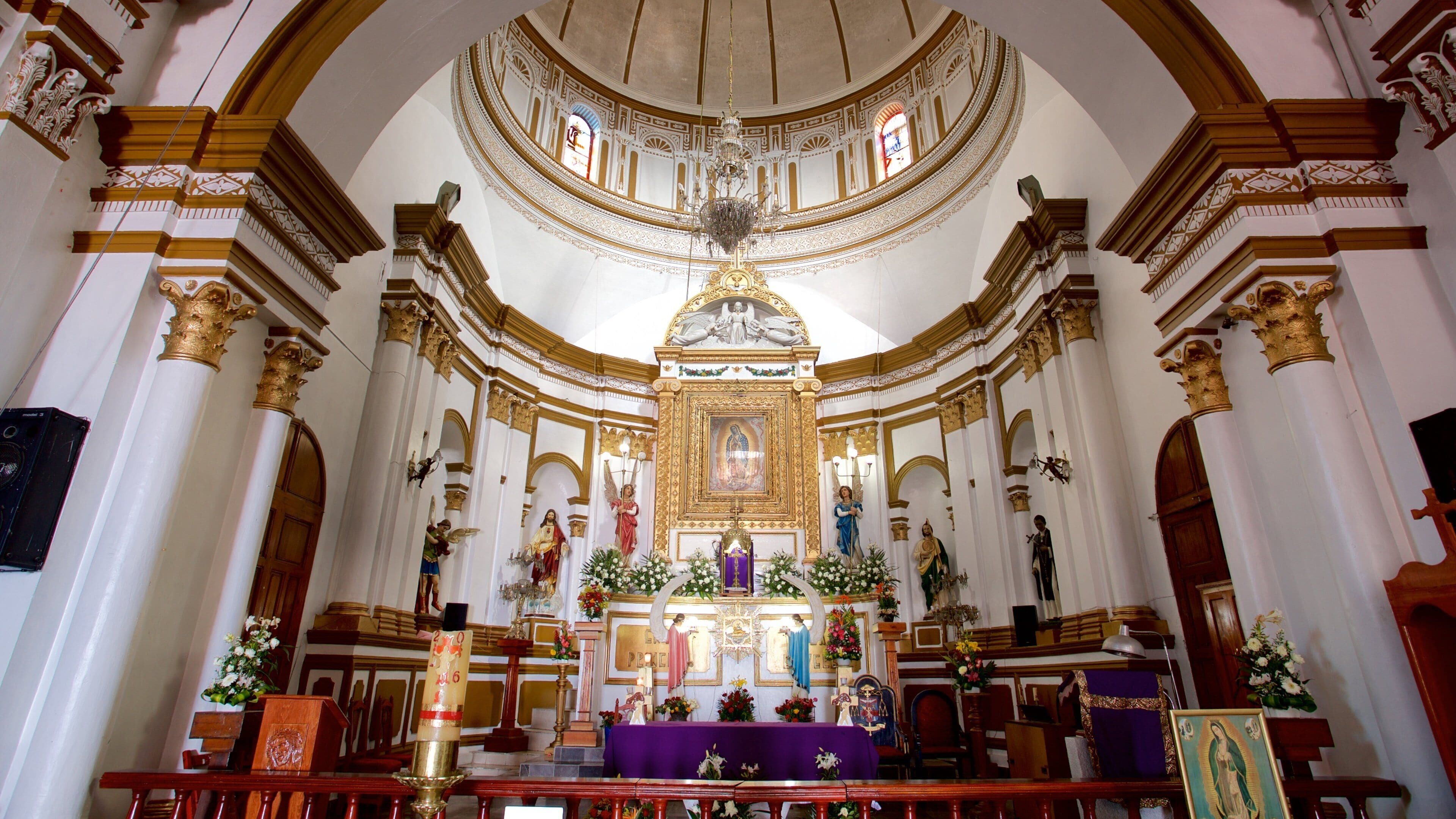 An ornate church interior with a central altar, statues, and a dome ceiling.