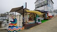 A colorful outdoor seating area with a rainbow mural, a small stage, and a cafe in the background.