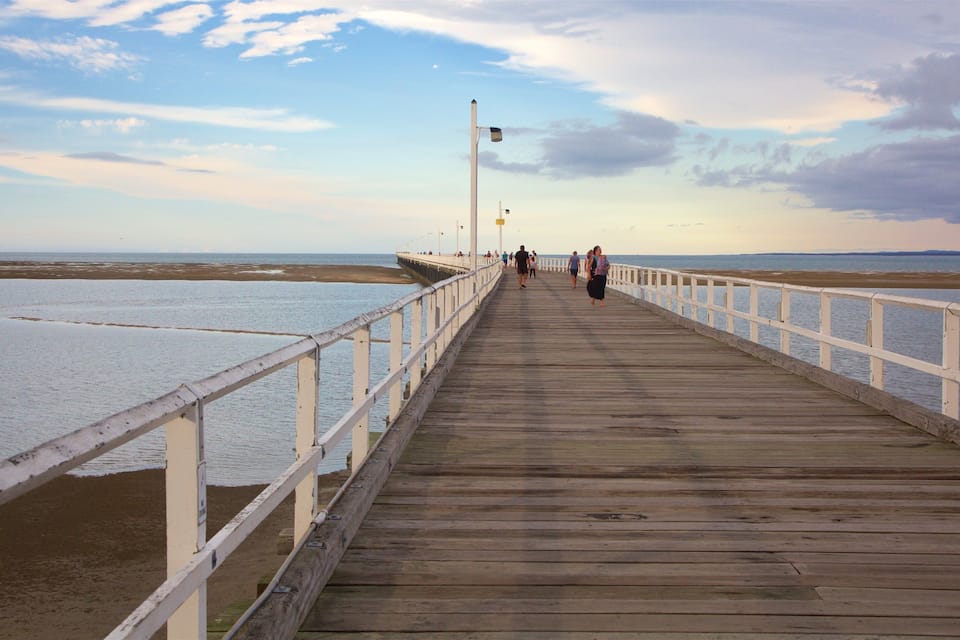 A wooden pier extending into calm waters with a white railing, under a partly cloudy sky.