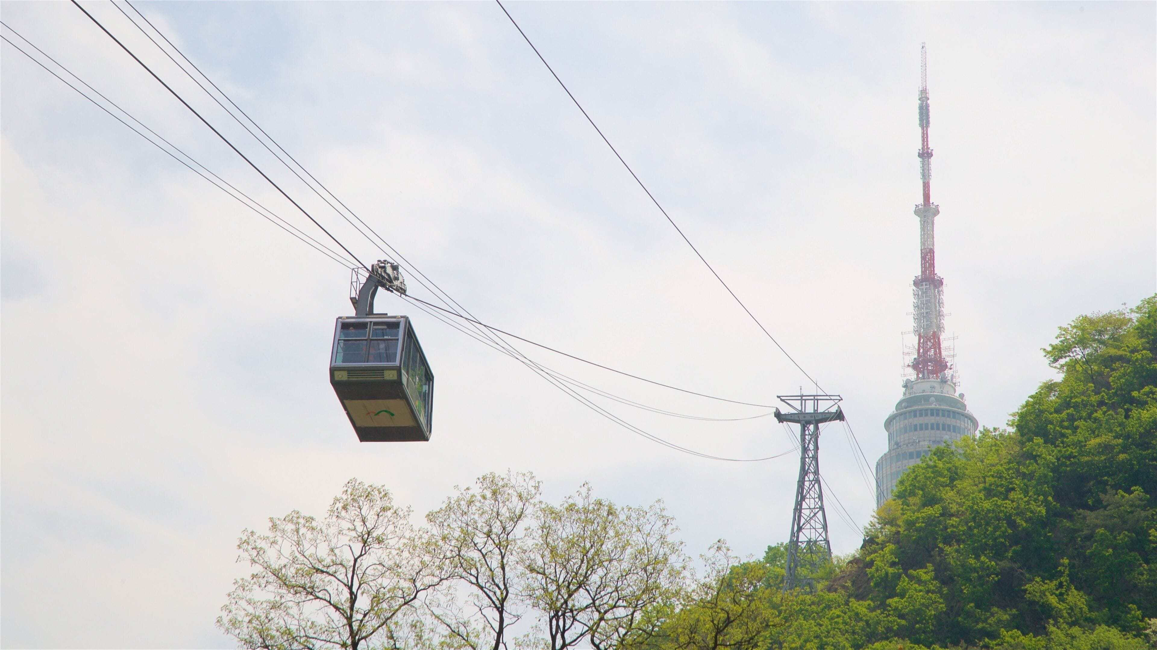 A cable car moving through the air with a tall tower in the background.