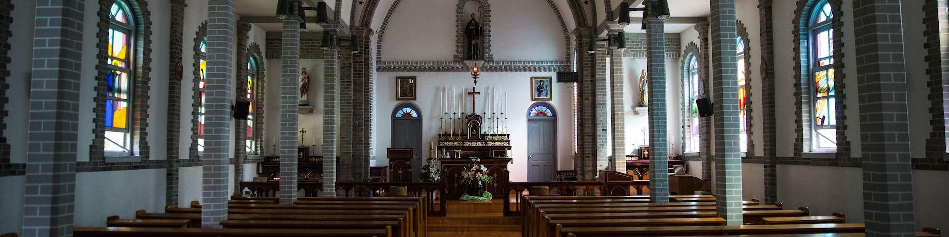 An interior of a church with wooden pews, arched ceilings, and stained glass windows.