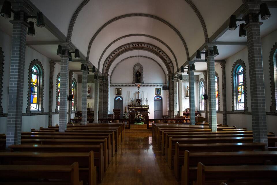 Interior de uma igreja com bancos de madeira, tetos abobadados e vitrais.