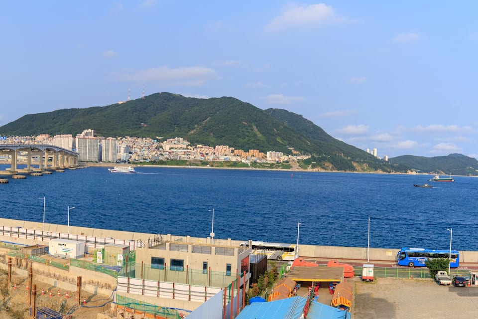 Un paysage urbain côtier avec un pont, un chantier de construction et une montagne en arrière-plan.