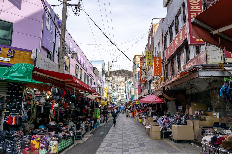A narrow street with various shops on either side, displaying hats and other merchandise.