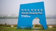 A blue sign with Korean text for Yeouido Hangang Park, a river, and a city skyline in the background.
