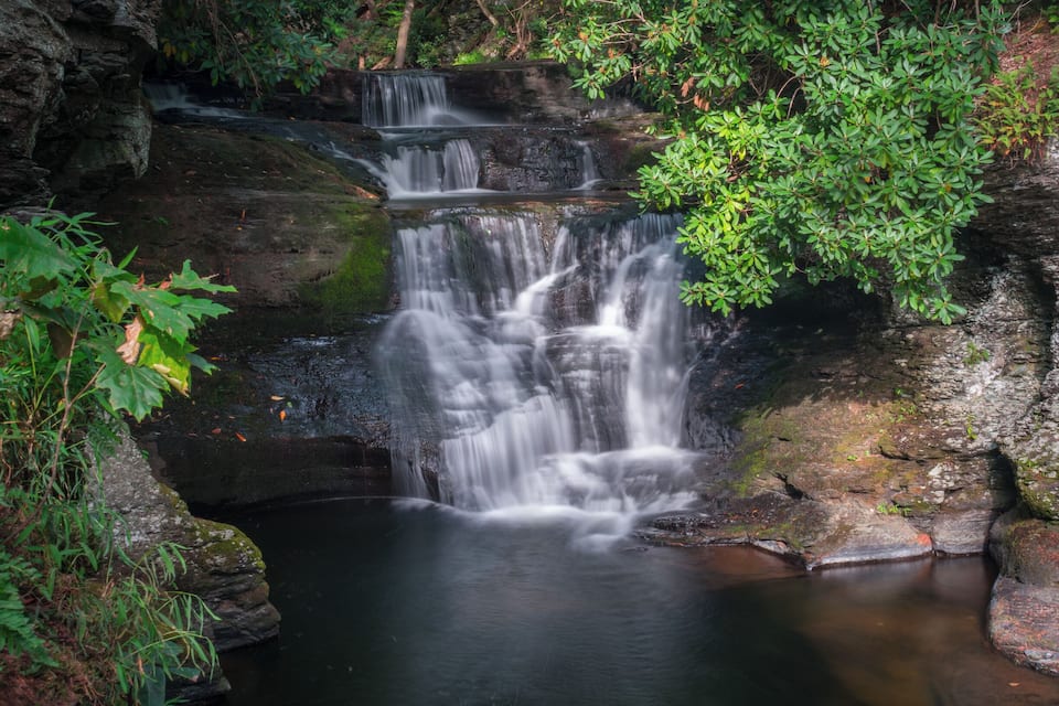 A waterfall cascading over rocks into a pool, surrounded by lush greenery.