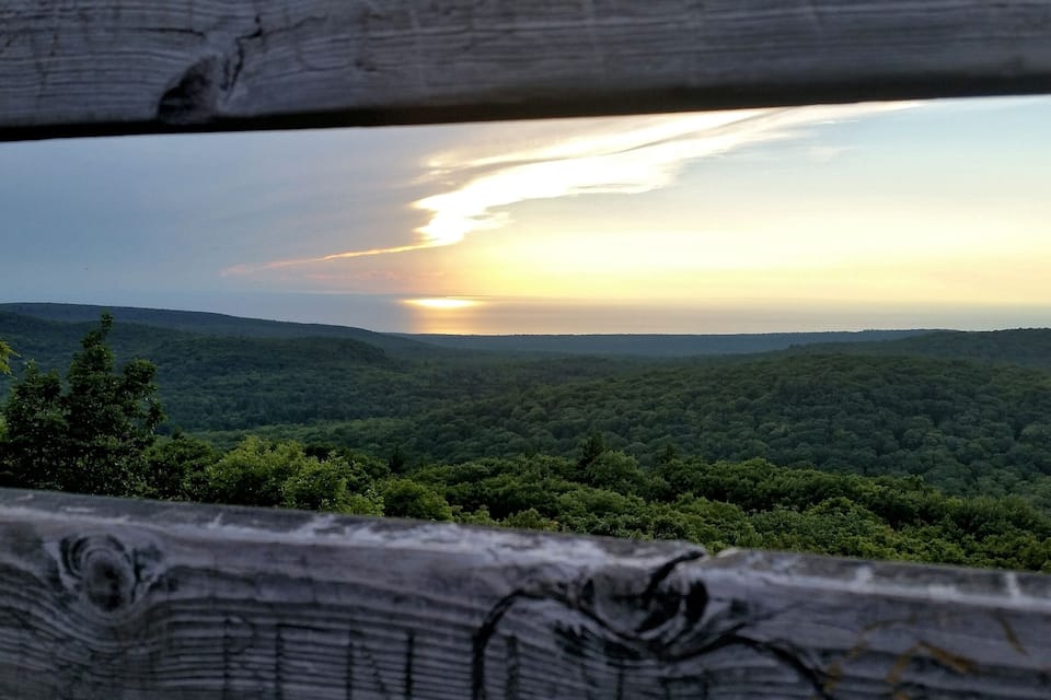 A sunset over a forested landscape with a wooden fence in the foreground.