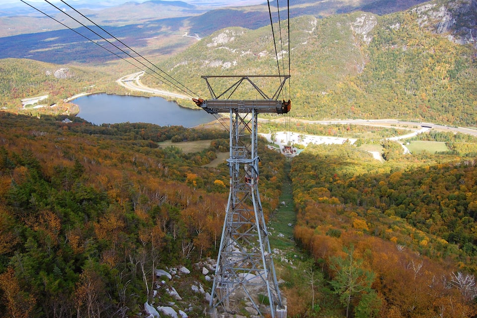 A cable car system in a mountainous area with autumn foliage, a lake, and a winding road.