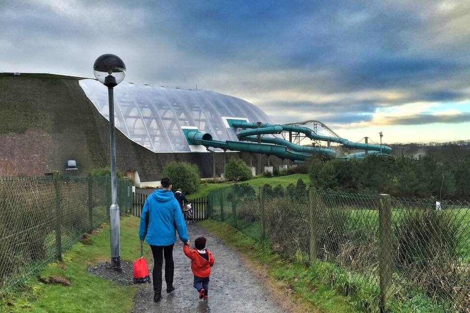 A pathway leading to a large, transparent building with a green water slide.