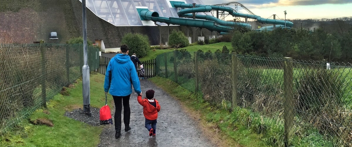 A pathway leading to a large, transparent building with a green water slide.