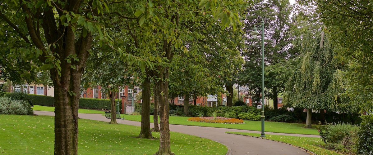 A curved pathway in a park with trees and a brick building in the background.