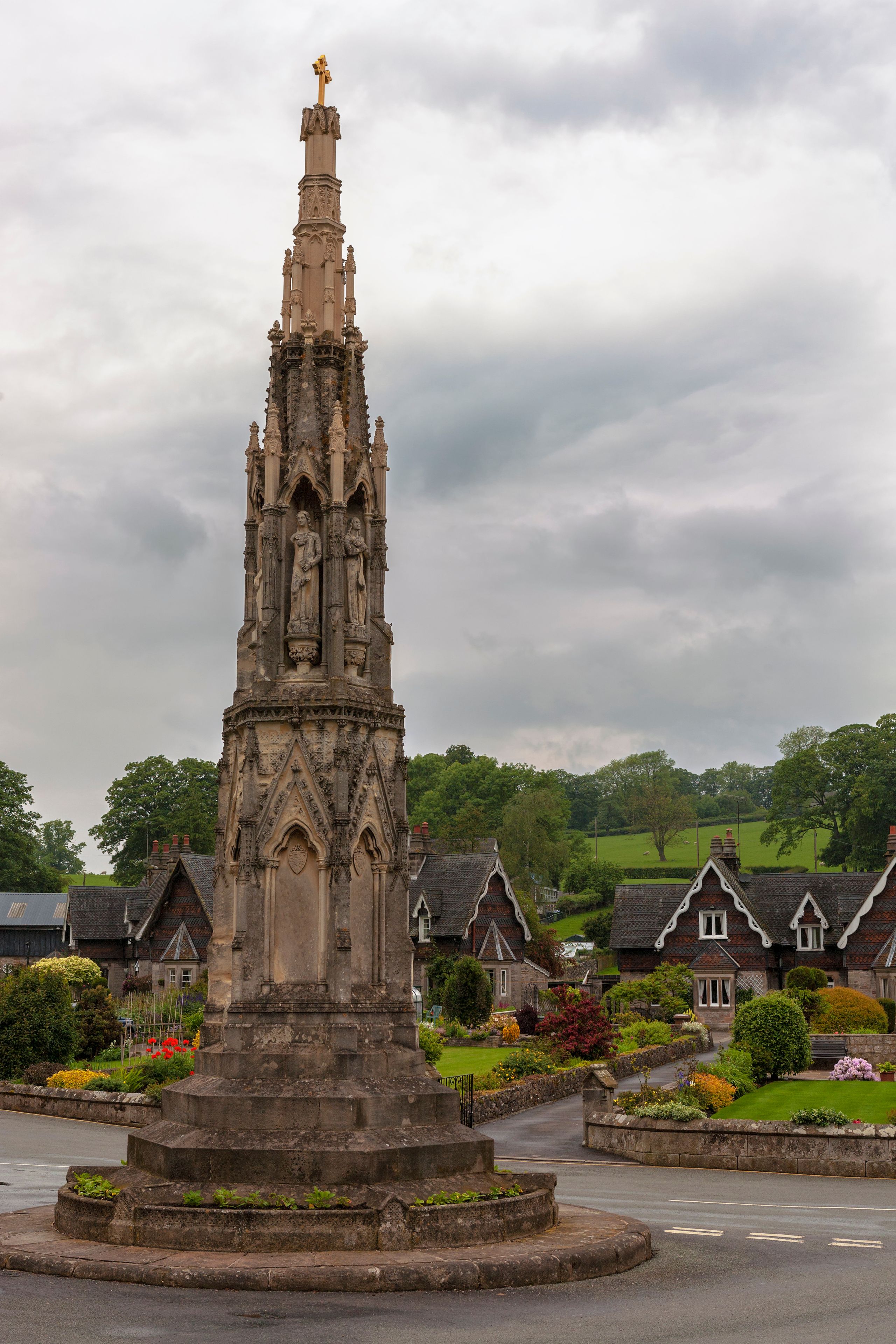 A Gothic-style church tower with intricate stone carvings and statues, surrounded by traditional houses and lush greenery.