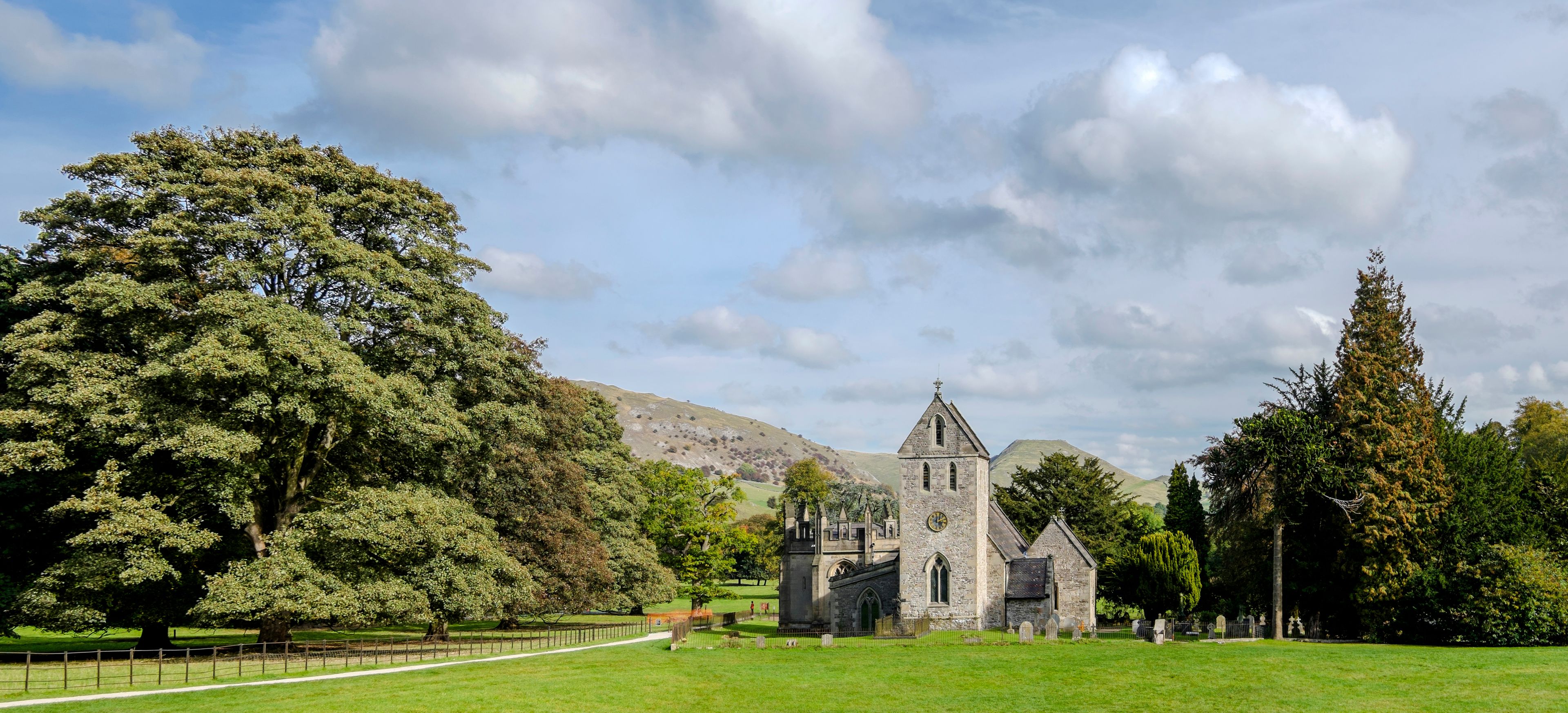 A historic stone church with a tower, surrounded by lush green grass and trees.