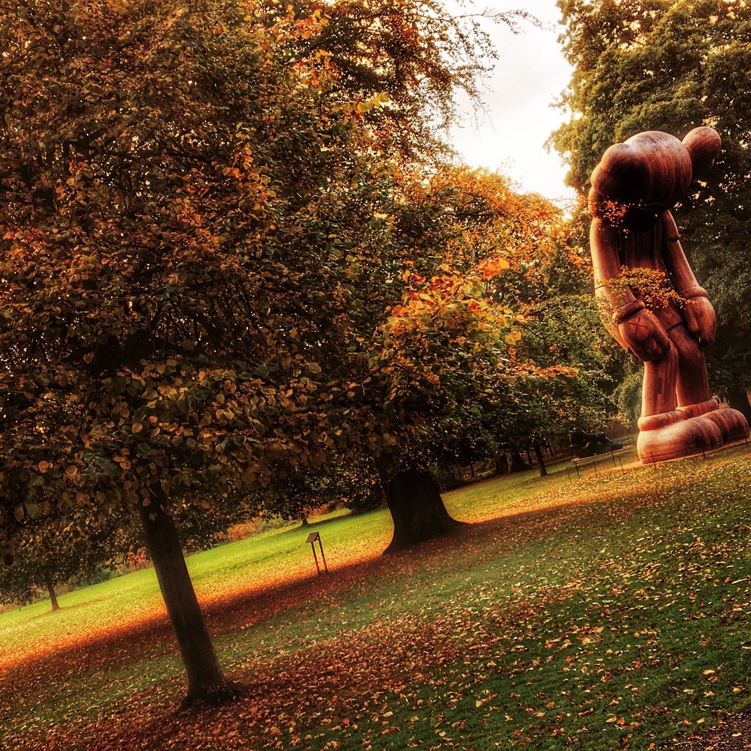 A park with autumn trees, a large sculpture, and a grassy area.