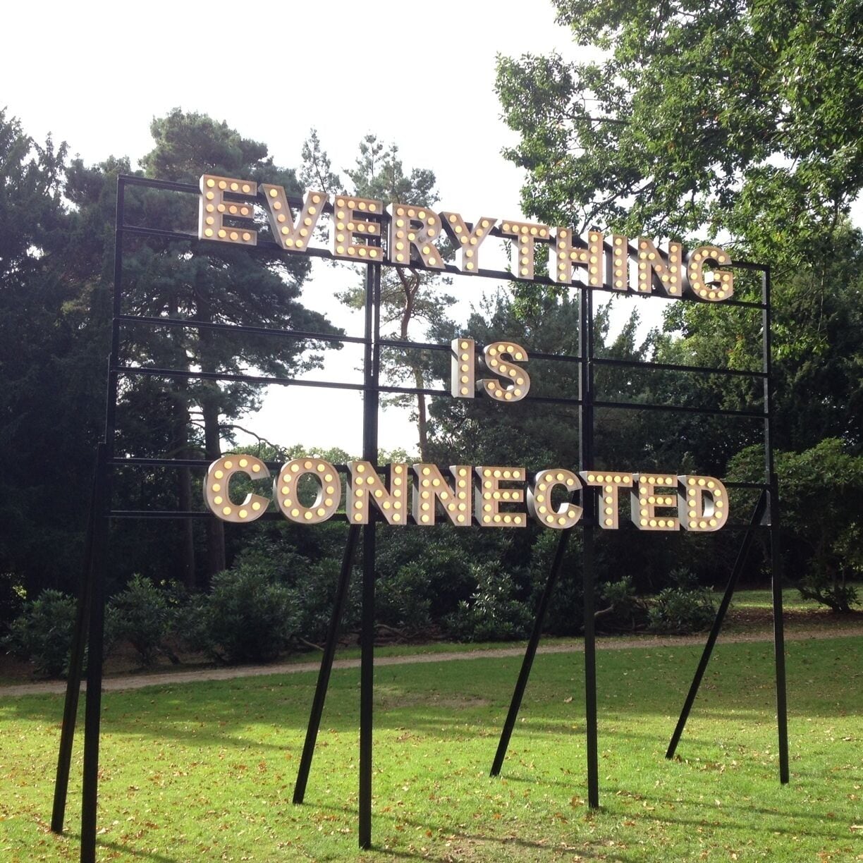 A sign with illuminated letters stating "EVERYTHING IS CONNECTED" in a park setting.