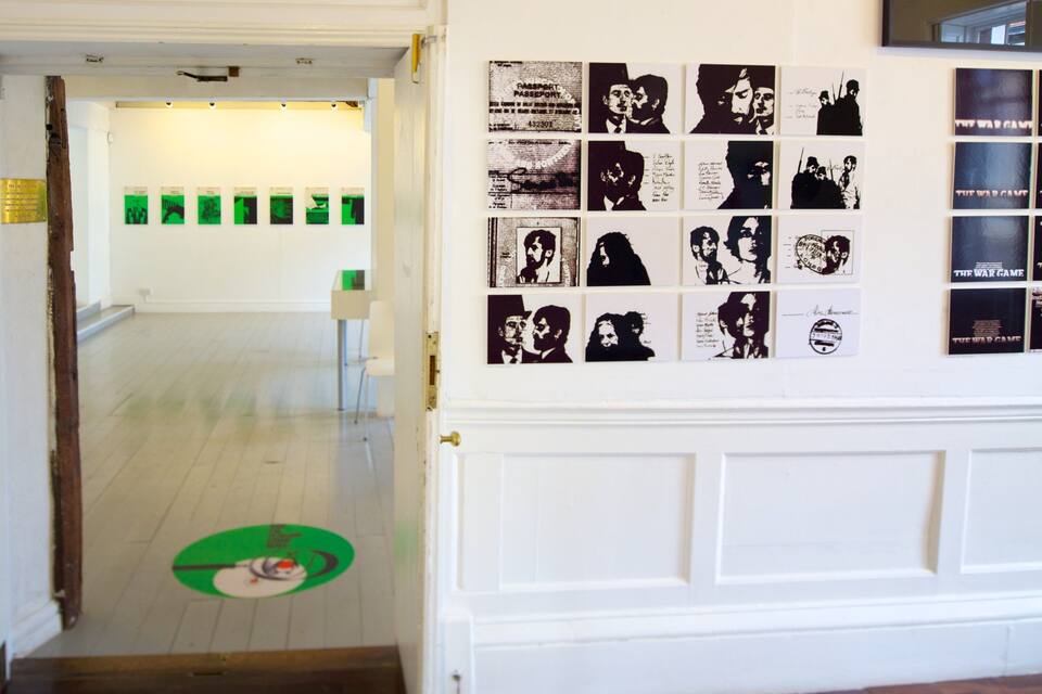Un pasillo con una puerta blanca, marcas en el suelo color verde y una pared con carteles blanco y negro.
