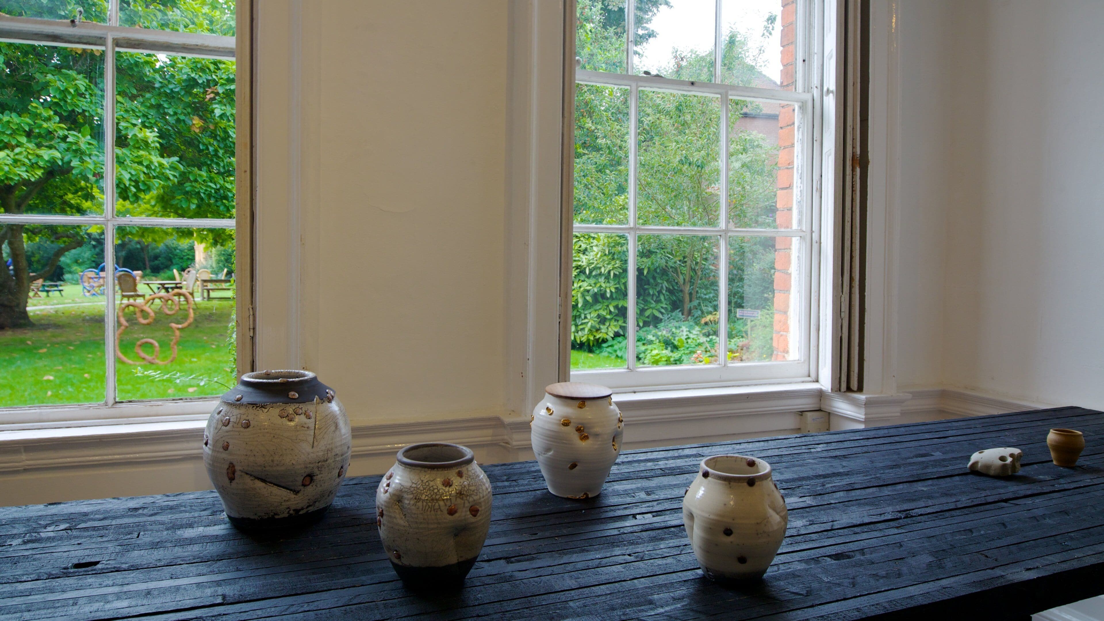 Four ceramic pots on a wooden table by a window overlooking a garden.