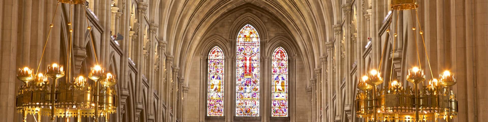 A cathedral interior with Gothic architecture, stained glass windows, and ornate chandeliers.