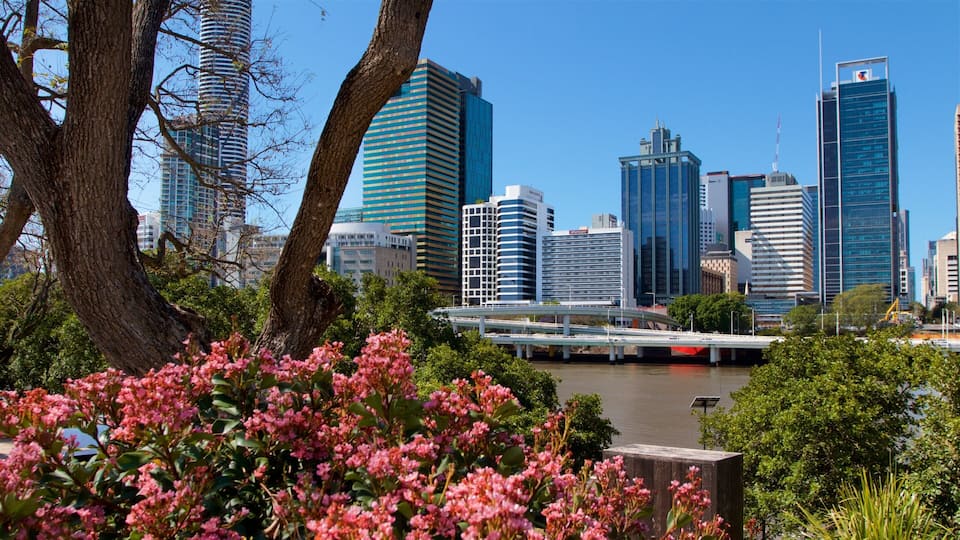 A city skyline with modern skyscrapers, a river, and lush greenery in the foreground.
