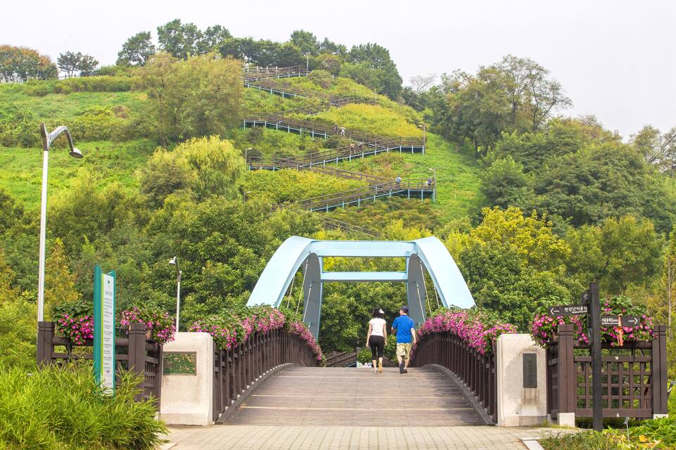 Uma ponte com arco azul, cercada por vegetação e flores cor-de-rosa.