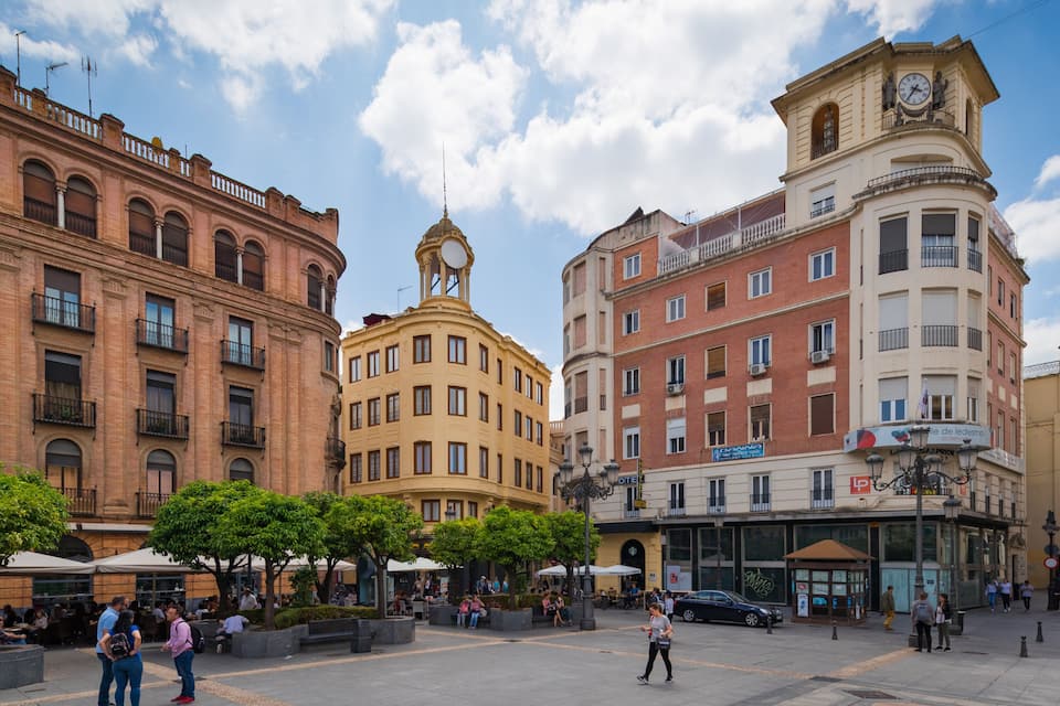 En livlig plads med historiske bygninger, blandt andet et tårn med et ur og en café.