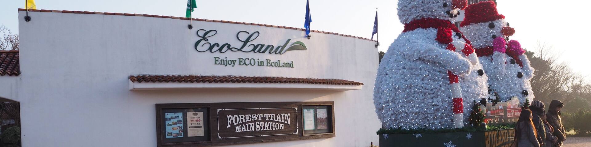 Un edificio con letreros de 'EcoLand', un cartel que dice 'Estación Principal del Tren Forestal' y dos decoraciones de muñeco de nieve.