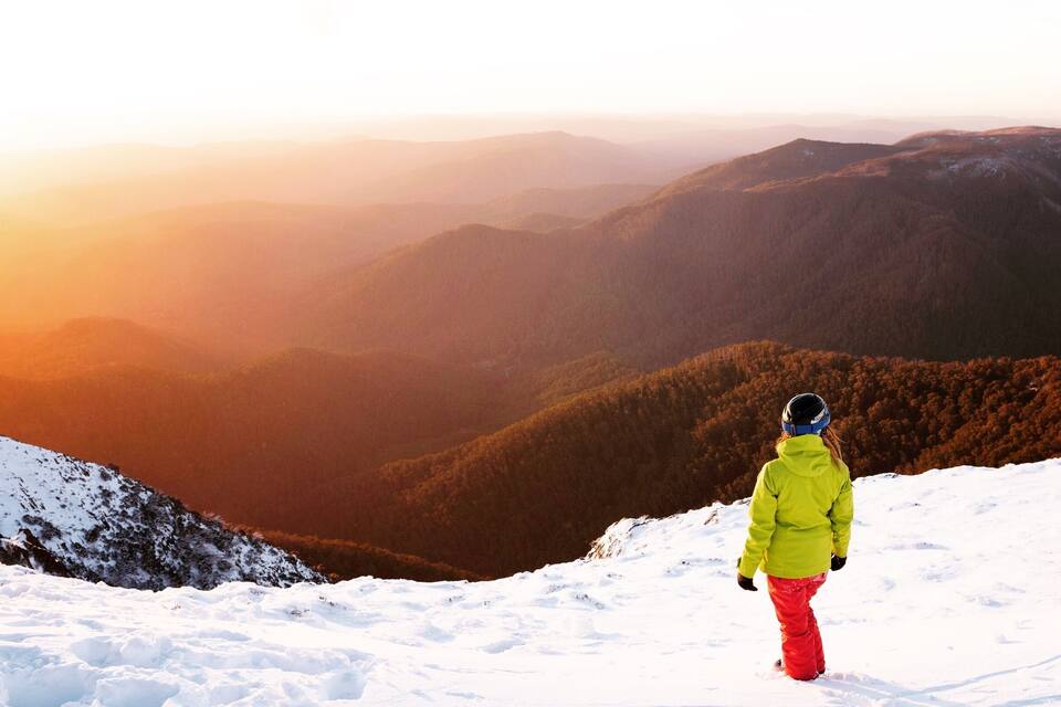 A person skiing on a snowy mountain slope with a view of forested valleys and distant mountains.