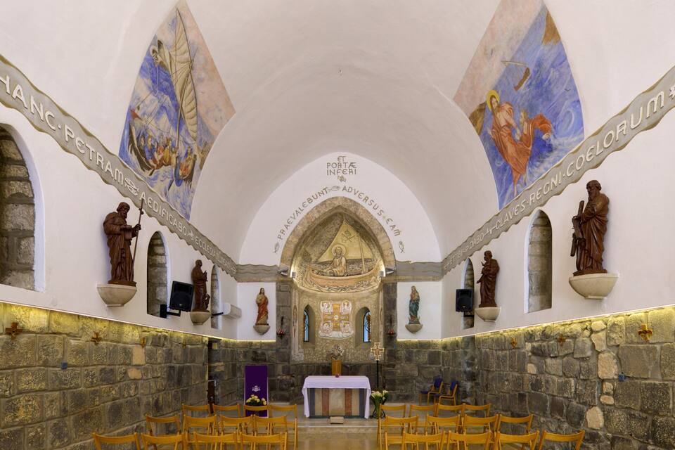 An interior of a church with stone walls, wooden pews, and religious statues.