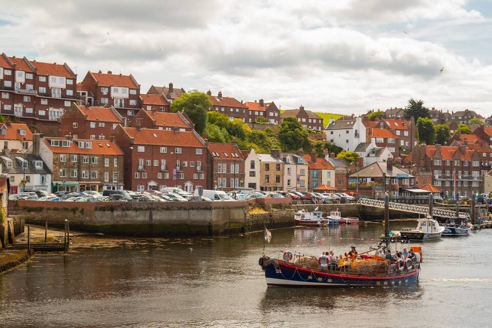 A harbor with a red-roofed boat docked at the pier, surrounded by historic buildings and a cloudy sky.