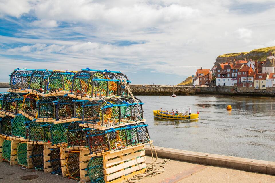 A harbor with colorful lobster traps, a boat, and historic buildings on a hill.