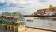 Un port où l’on peut admirer des casiers à homards aux couleurs vives, un bateau et des bâtiments historiques situés sur une colline.