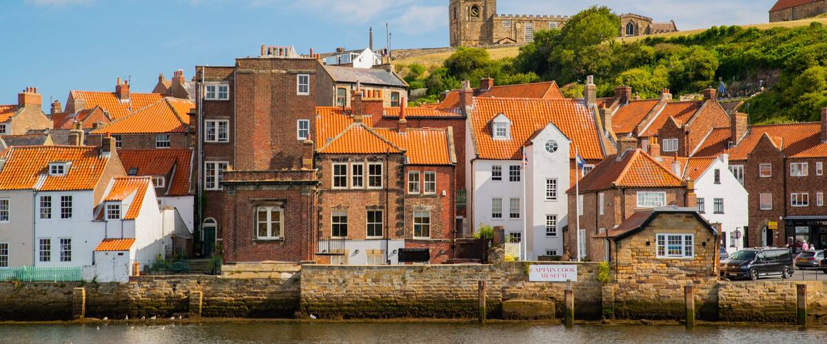 A waterfront town with red-tiled roofs, a stone wall, and a castle in the background.