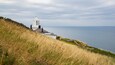 A coastal lighthouse on a grassy cliff overlooking the sea.