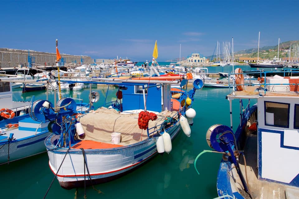 A marina with various boats docked, including a blue and white boat with a covered deck and a red and white boat with a cabin.