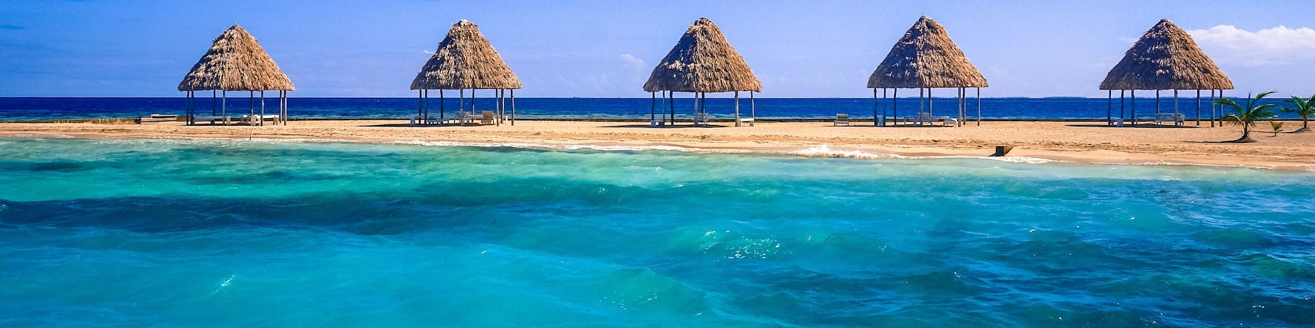 A row of thatched palapas on golden sand on the tiny island of Rendezvous Caye in the Belize Barrier Reef, off the coast of Belize, Central America