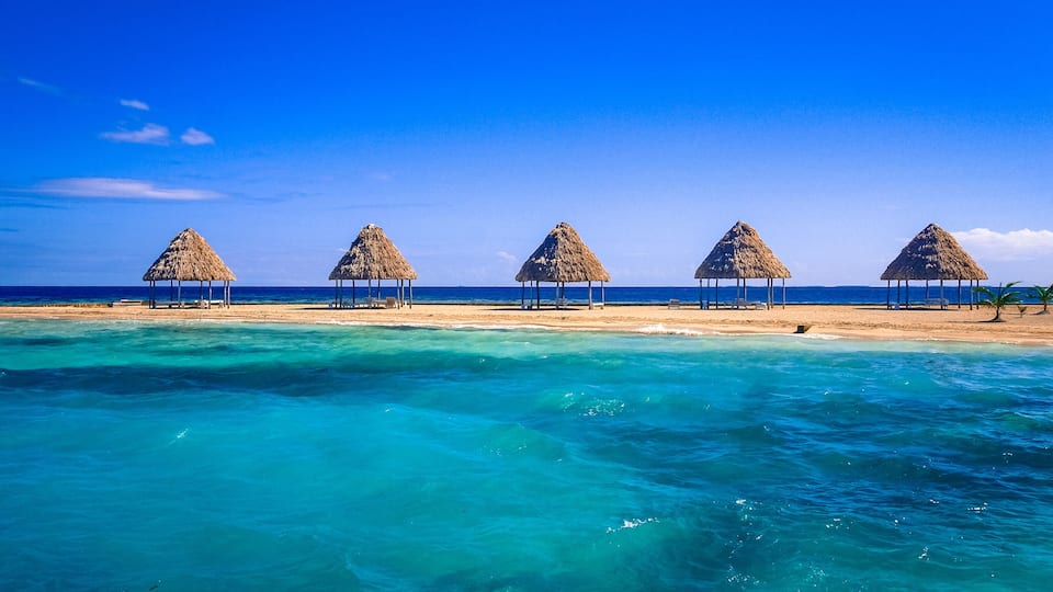 A beach with thatched-roof huts and clear turquoise waters.