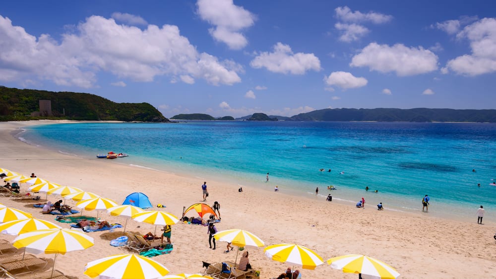 A beach with clear turquoise water, sandy shore, and several yellow and white umbrellas.